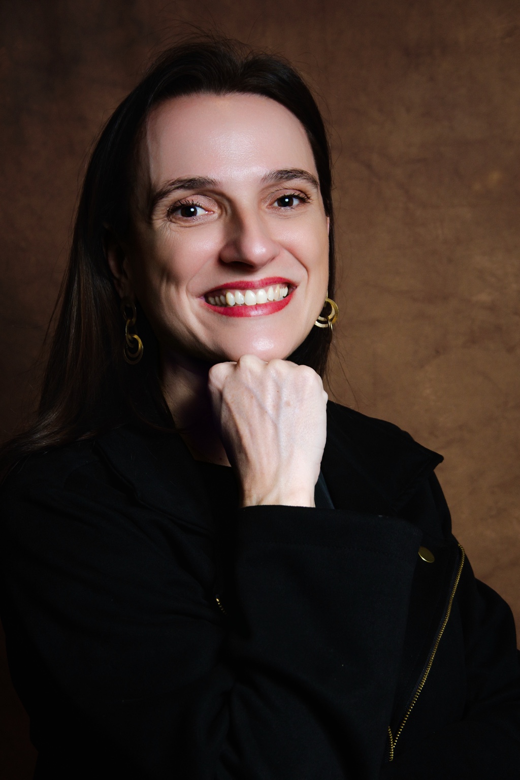 Liana Vertuan sorrindo, com a mão apoiada no queixo
